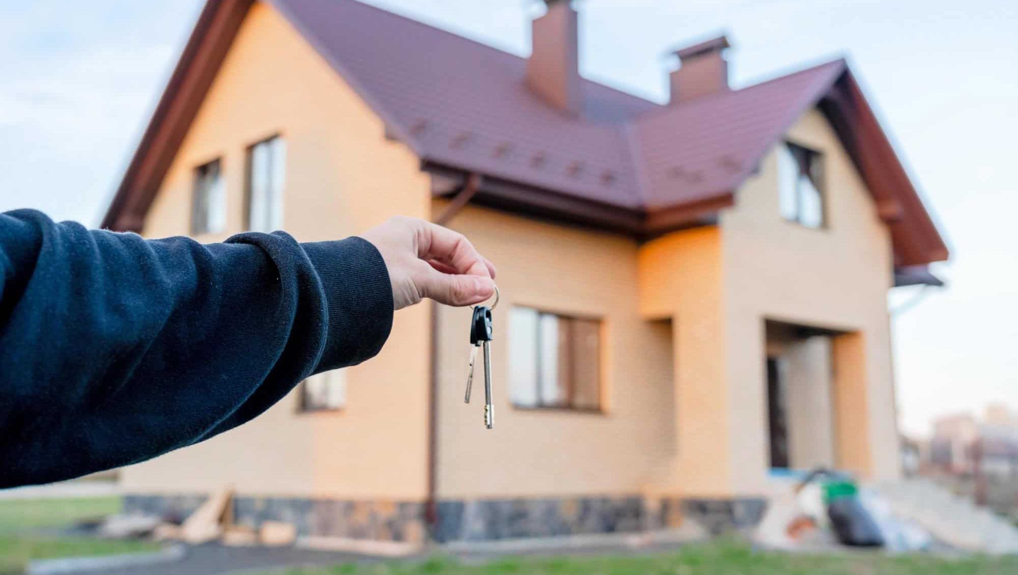 En hånd holder nøkler foran et ferdigstilt hus med rødt tak.