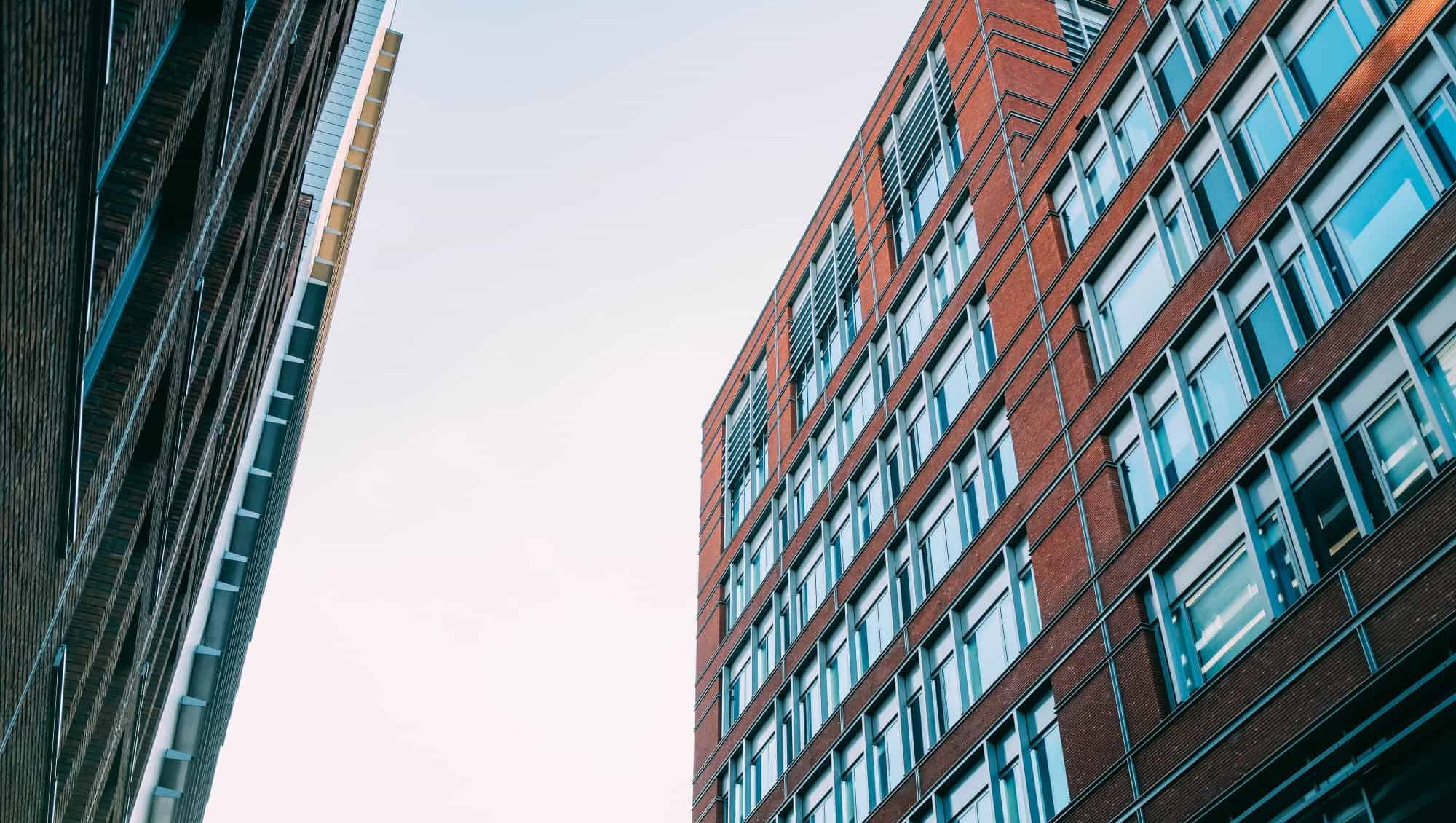 Moderne kontorbygg i murstein og glass sett fra gateplan med himmel i bakgrunnen.